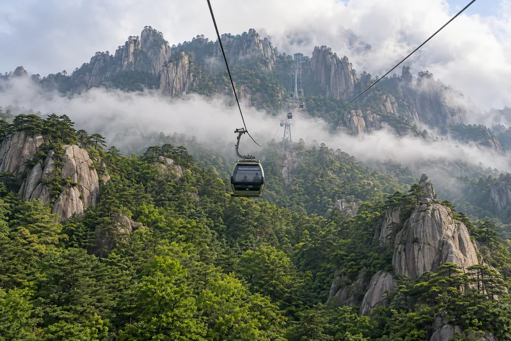A Yungu cable car cabin climbing over forested granite ridges toward the summit of Huangshan