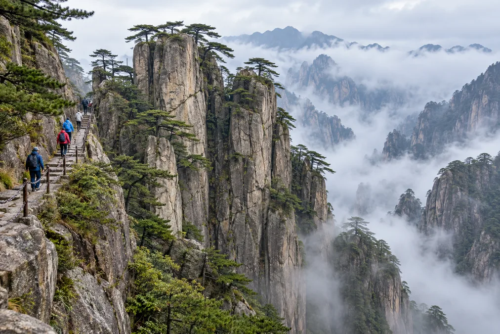 Pines on steep granite pillars near Beginning-to-Believe Peak, with a stone stairway along the cliff and mist in the gorge below
