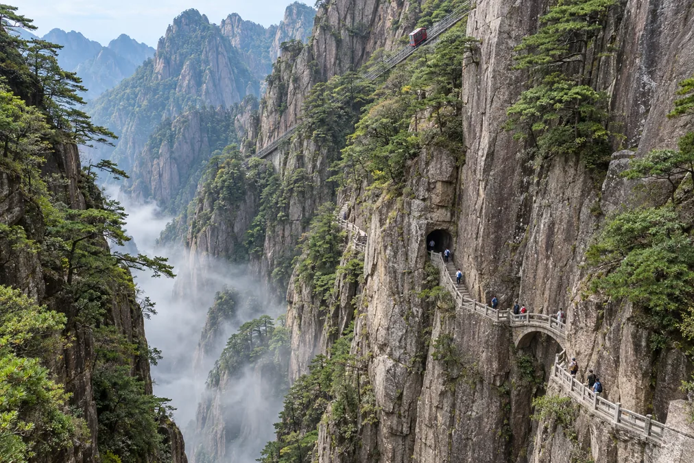 Cliff-side stone paths winding through the West Sea Grand Canyon on Huangshan, with the sightseeing rail car track on the far slope