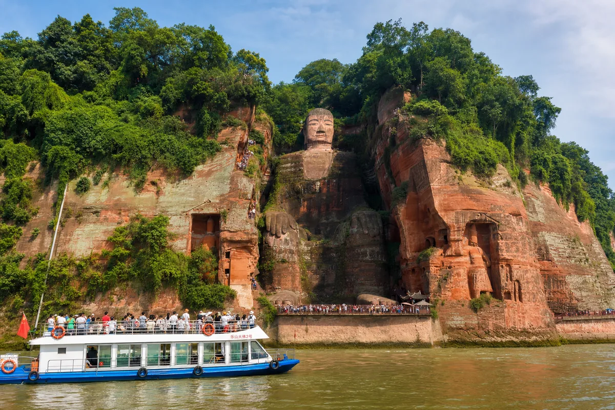 The Leshan Giant Buddha carved into the cliff with a tour boat on the river below