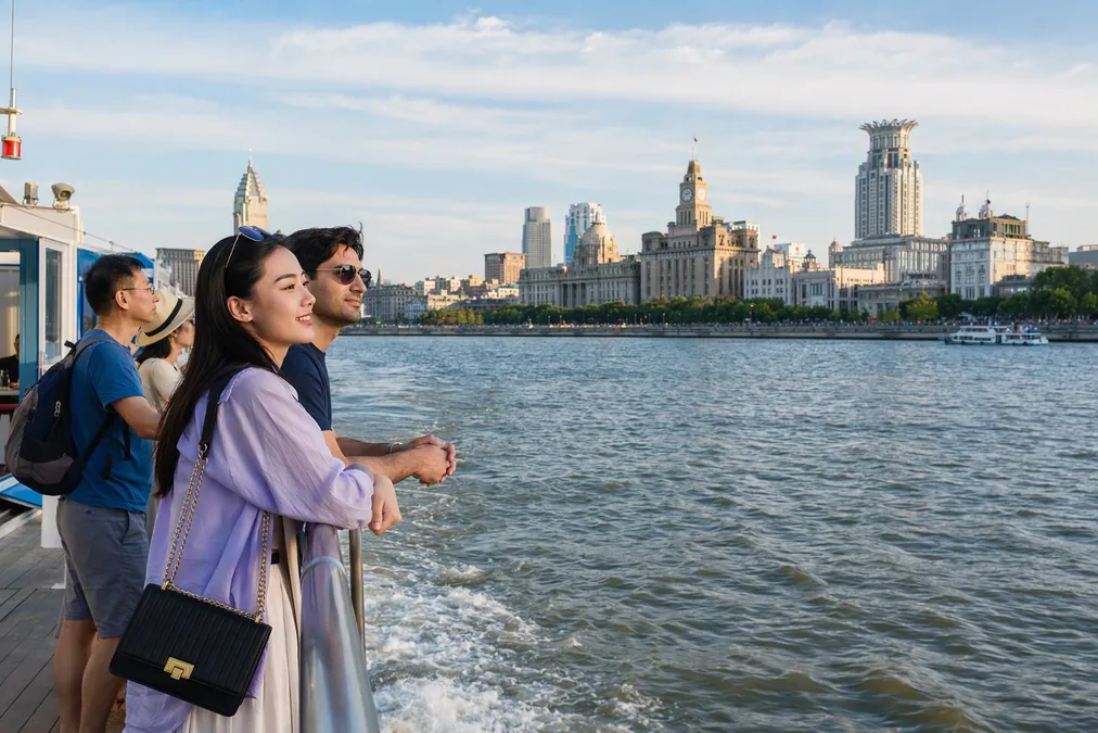 Passengers on the Huangpu River ferry deck approaching the Bund's historic waterfront