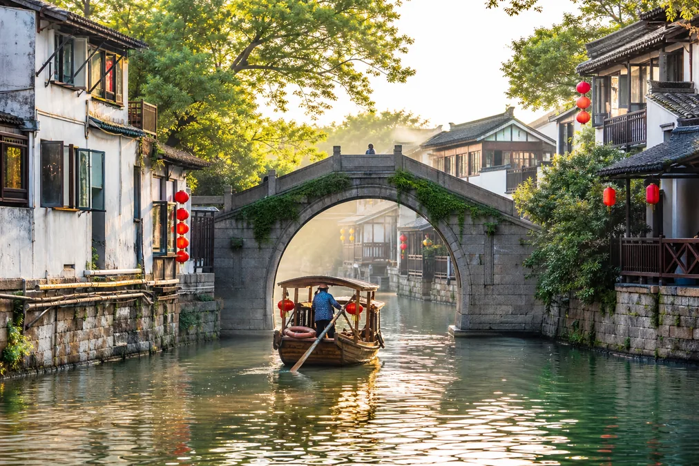 A rowing boat passing under a stone bridge on a quiet morning canal in Zhujiajiao water town