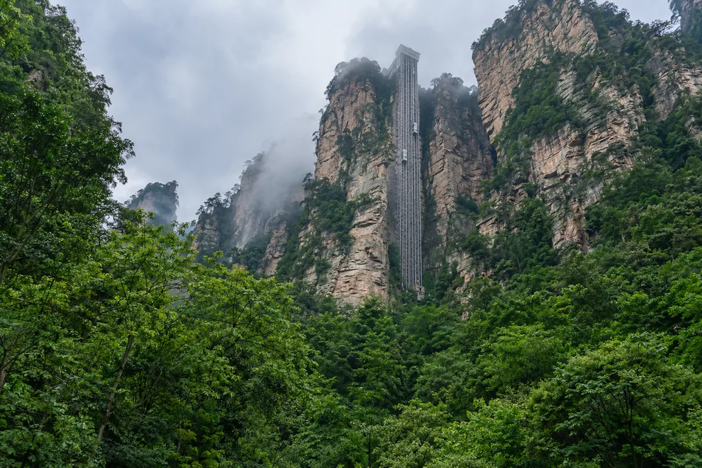 The Bailong Elevator shaft running up the outside of a sheer sandstone cliff in Wulingyuan, with forest at its base
