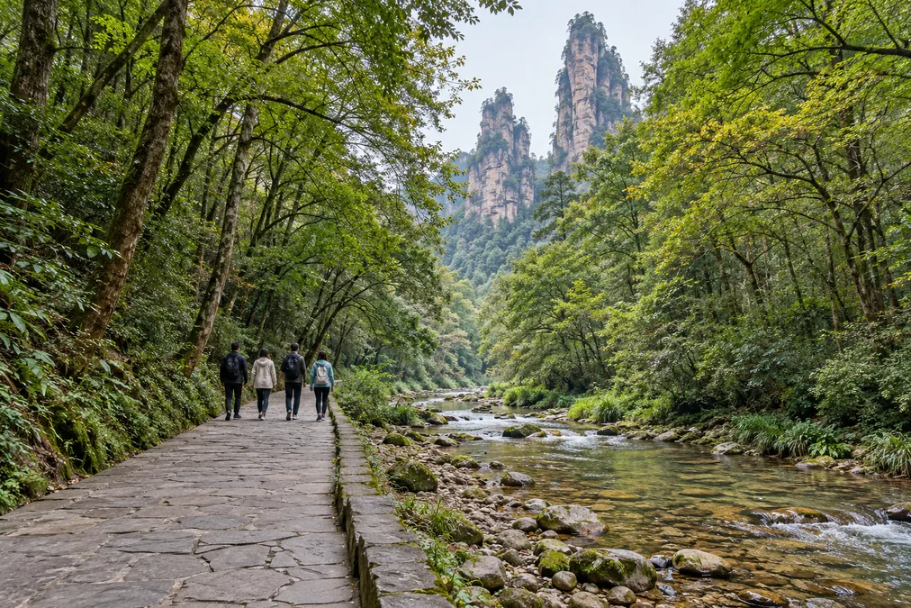 A paved path beside the clear, shallow Golden Whip Stream, with stone pillars rising above the trees