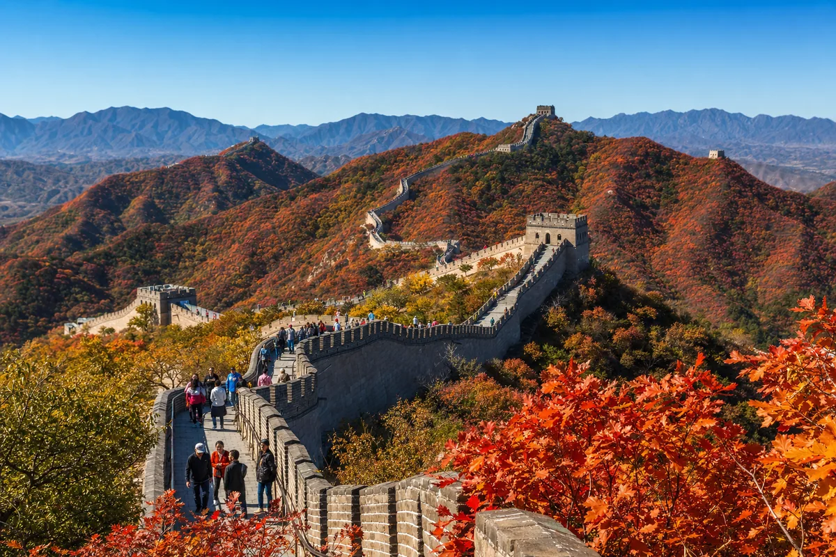 Great Wall of China winding through ridgelines covered in red autumn maple foliage near Beijing