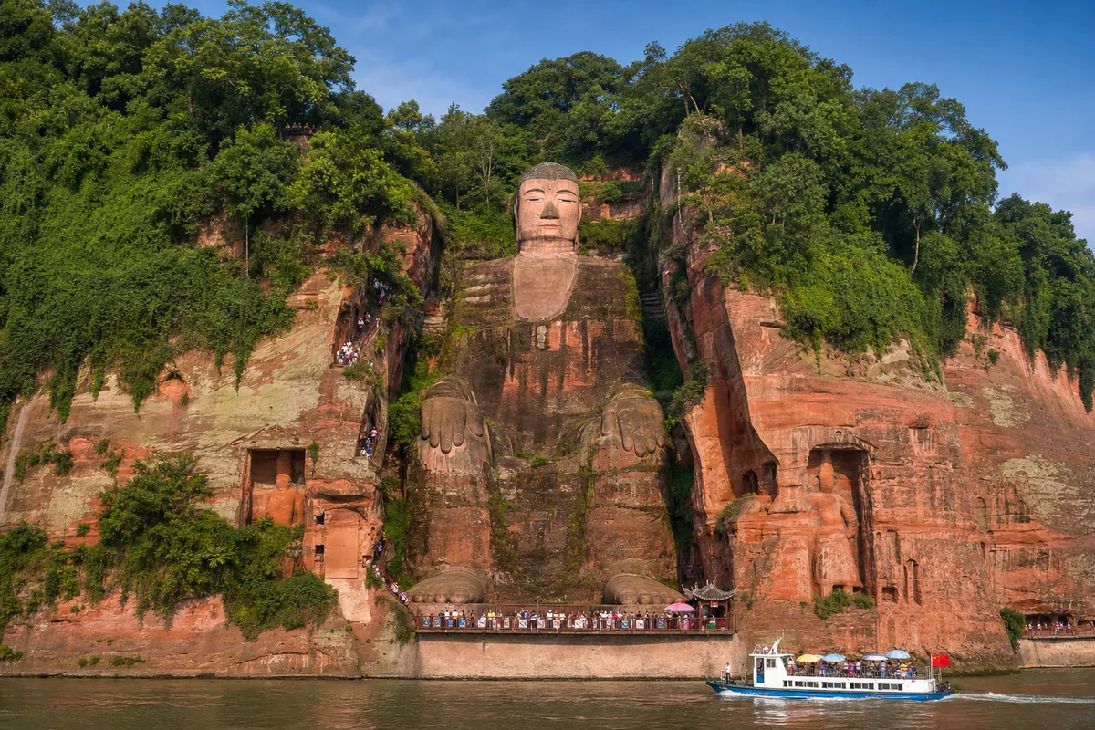 The Leshan Giant Buddha carved into a cliff with tiny visitors at its base for scale