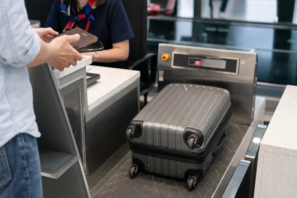 A suitcase on the scale at an airport check-in counter while a traveler holds a passport