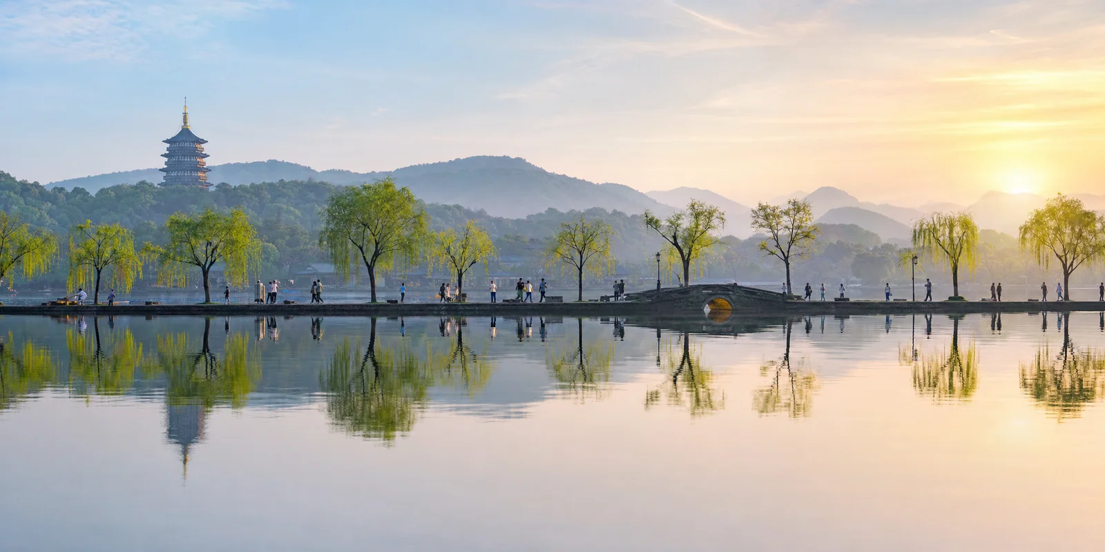 West Lake in Hangzhou at sunrise with a tree-lined causeway and distant pagoda across calm water