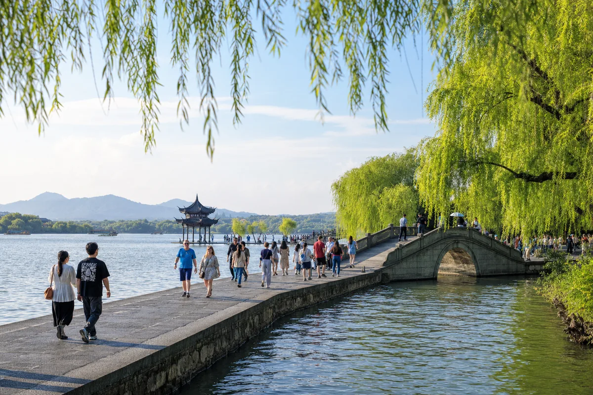 Visitors walking along a willow-lined causeway beside West Lake in Hangzhou