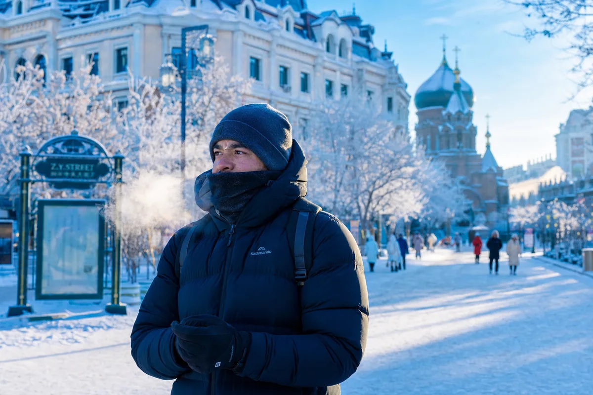 Traveler bundled in winter layers on a snowy Harbin street with frosted trees