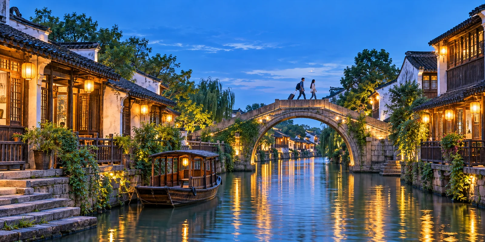 Wuzhen West Zone canal at dusk with a lit stone bridge, lantern-hung houses and two travellers crossing with a small suitcase