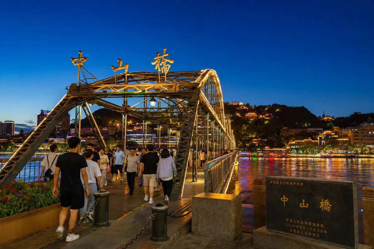 Pedestrians walking across the illuminated Zhongshan Bridge over the Yellow River in the evening