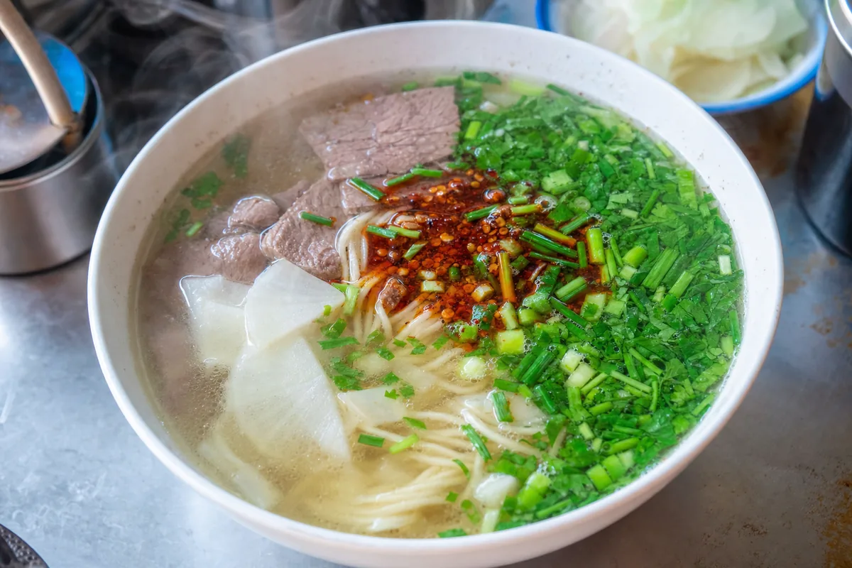 A bowl of authentic Lanzhou hand-pulled beef noodles with clear broth, chili oil, radish and beef slices