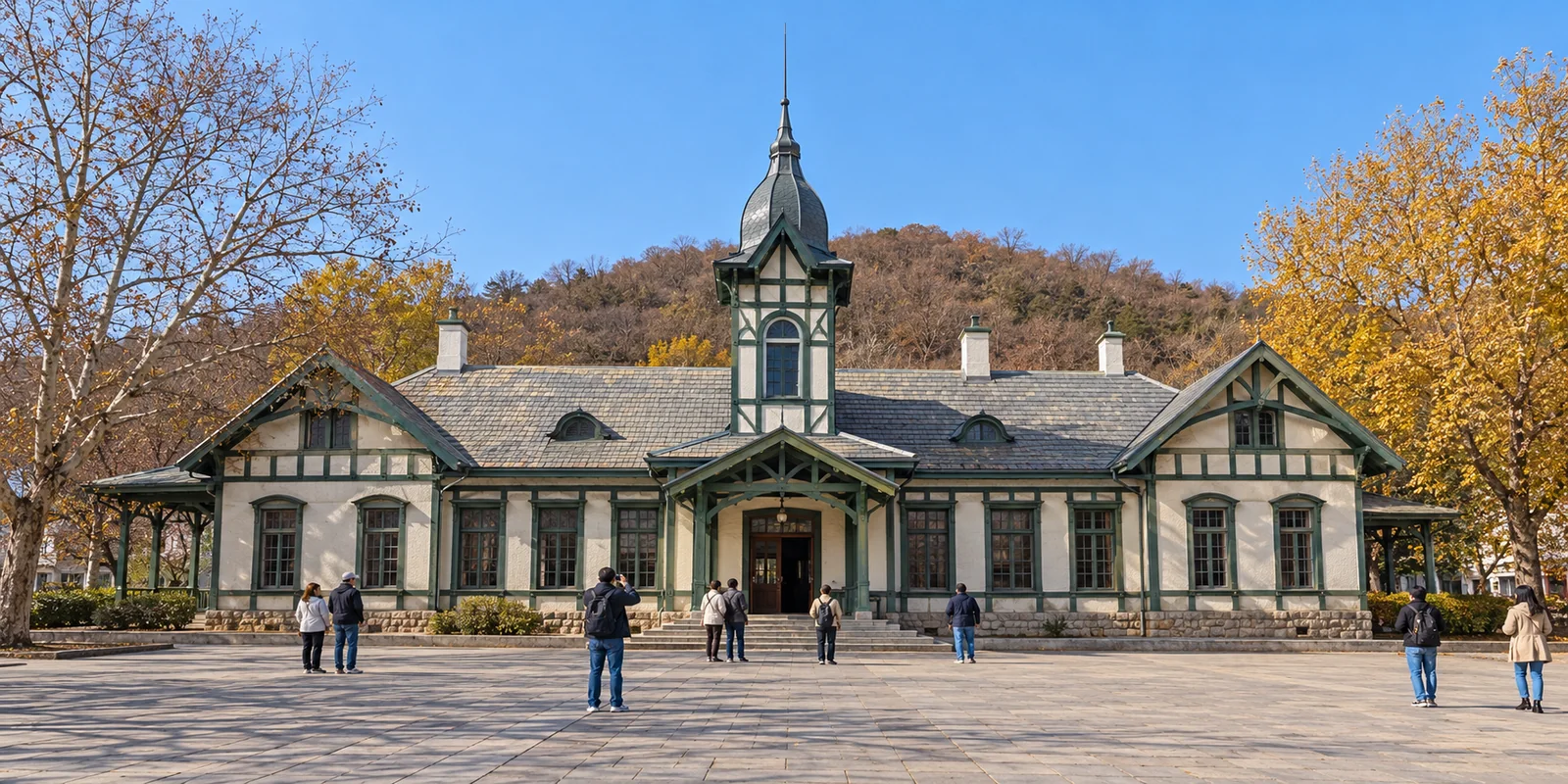 The historic Russian-style Lushun Railway Station building in Lushun, Dalian, under a clear autumn sky with a few visitors in front