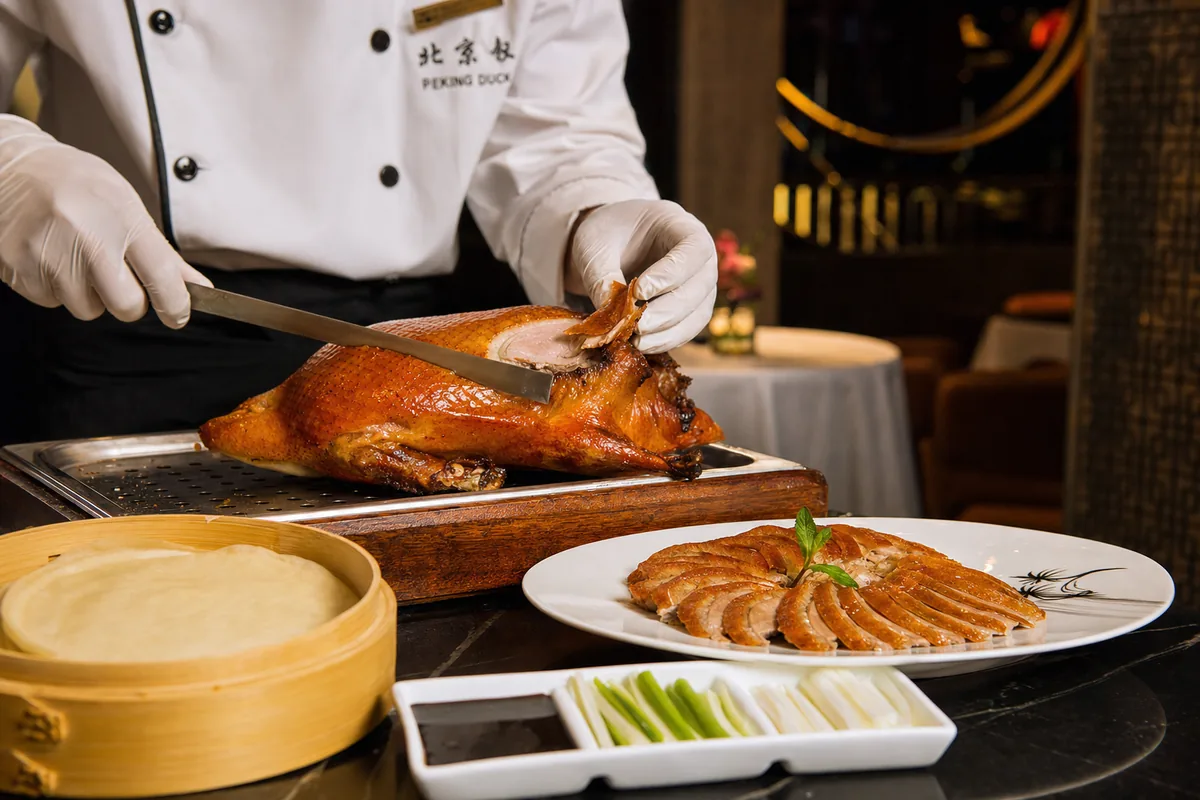 Chef carving crisp-skinned Peking duck tableside at an upscale Beijing restaurant