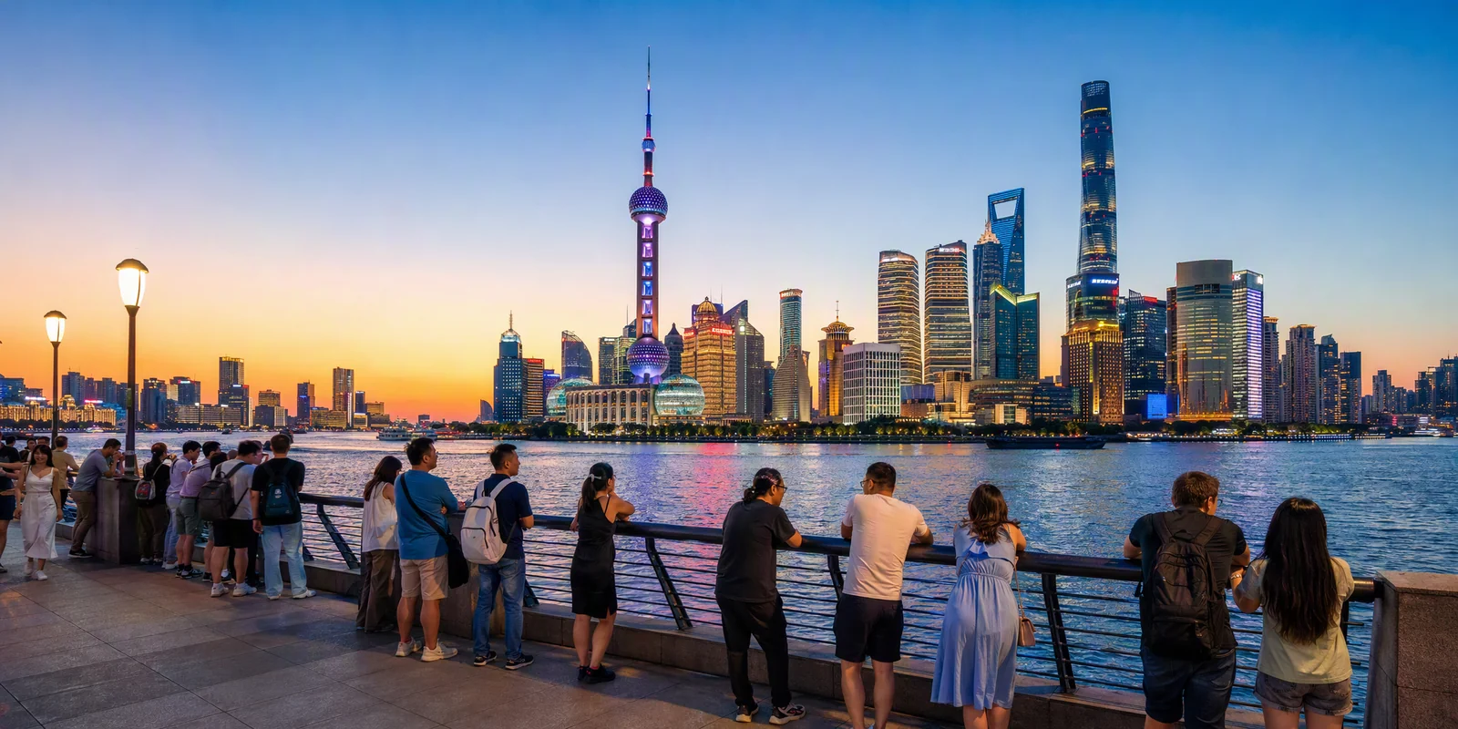 Visitors on the Bund promenade at dusk watching the lit-up Lujiazui skyline across the Huangpu River