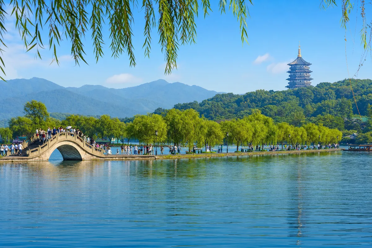 Hangzhou West Lake with a causeway, arched bridge and Leifeng Pagoda on a hill in the distance