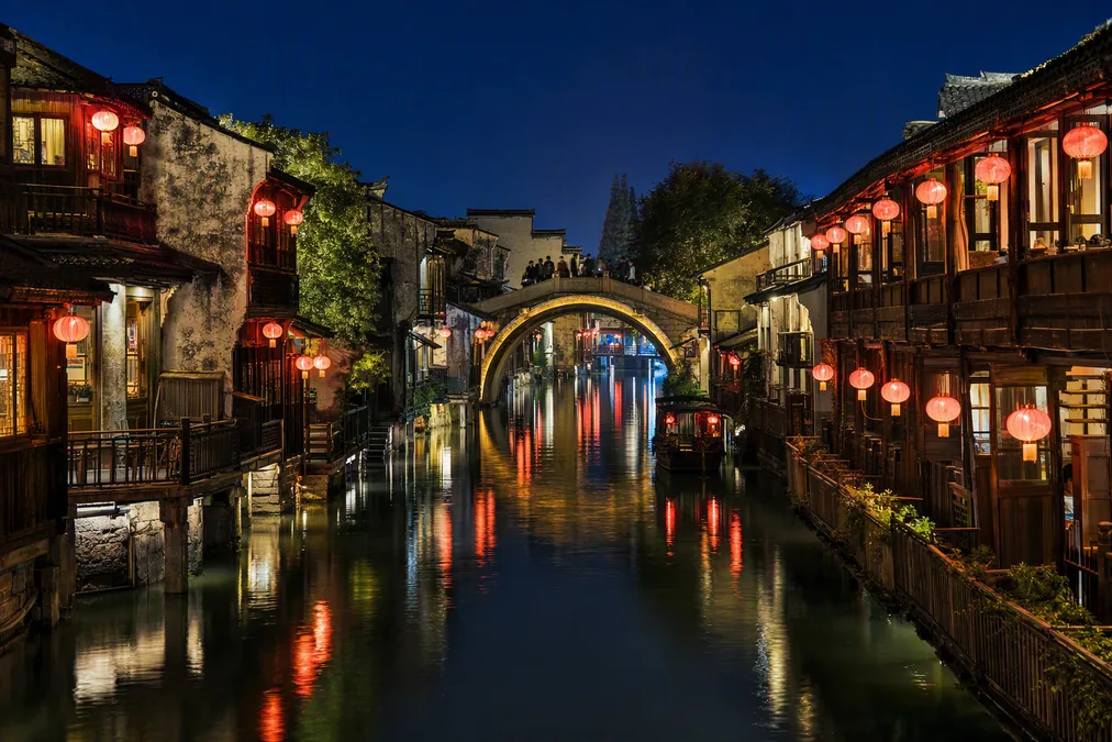 Lantern-lit canal and timber houses reflected in the water at night in Wuzhen's West Zone