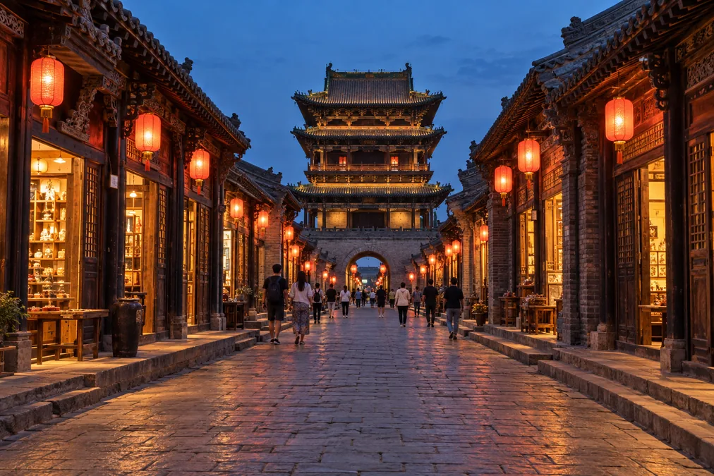 A stone street in Pingyao's old town lined with Ming and Qing shopfronts, the two-storey market tower spanning the street ahead