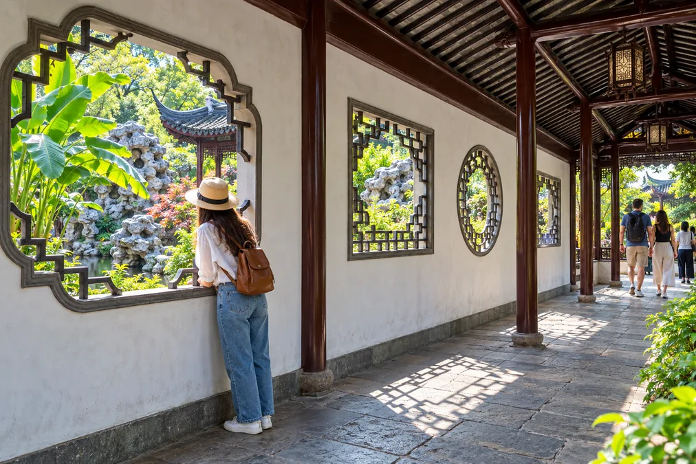 Covered walkway with lattice windows framing a rockery inside the Lingering Garden, Suzhou
