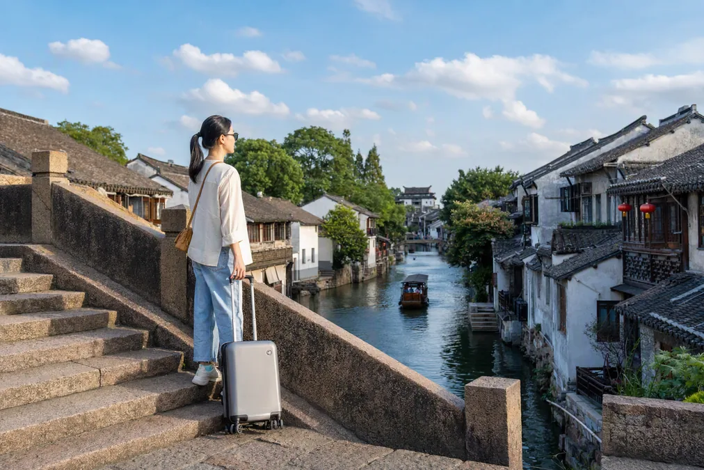 Traveler with a suitcase pausing on a stone bridge in a Chinese water town