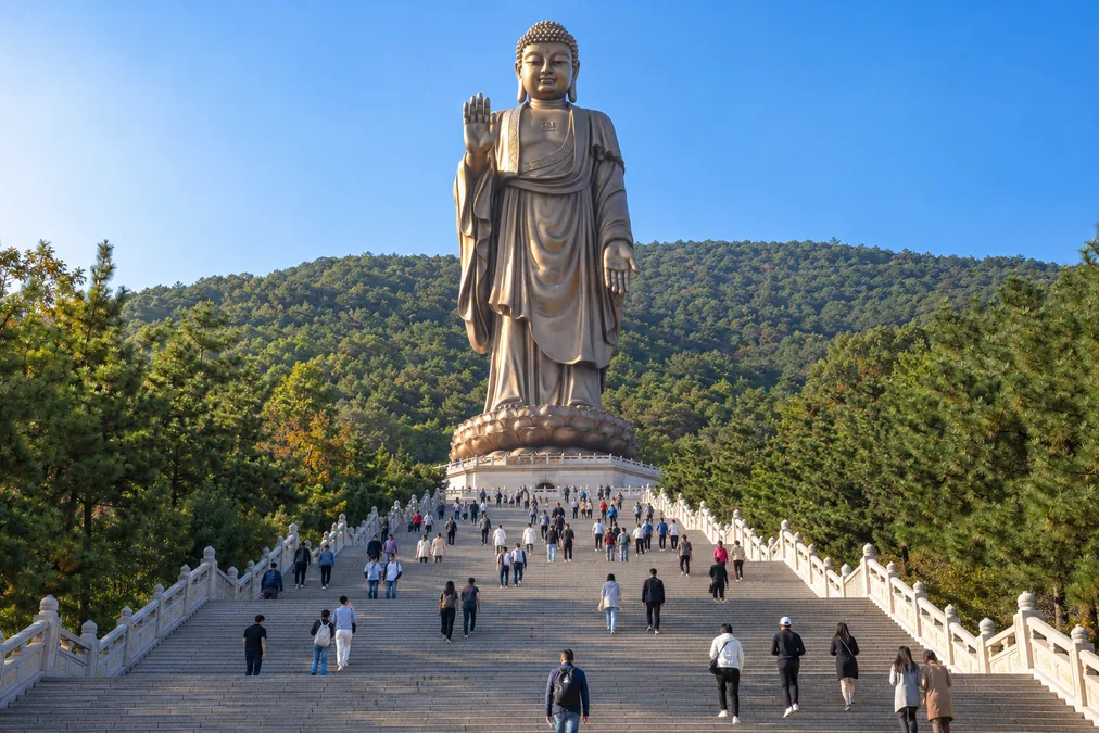 The bronze Lingshan Grand Buddha seen from the long stairway below, with visitors climbing towards its feet