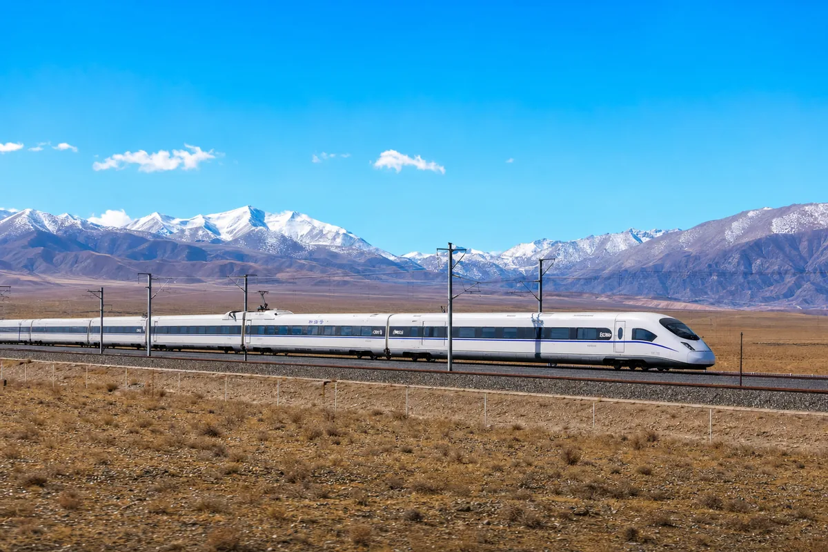 High-speed train crossing the arid Hexi Corridor toward Zhangye with snow-capped mountains behind